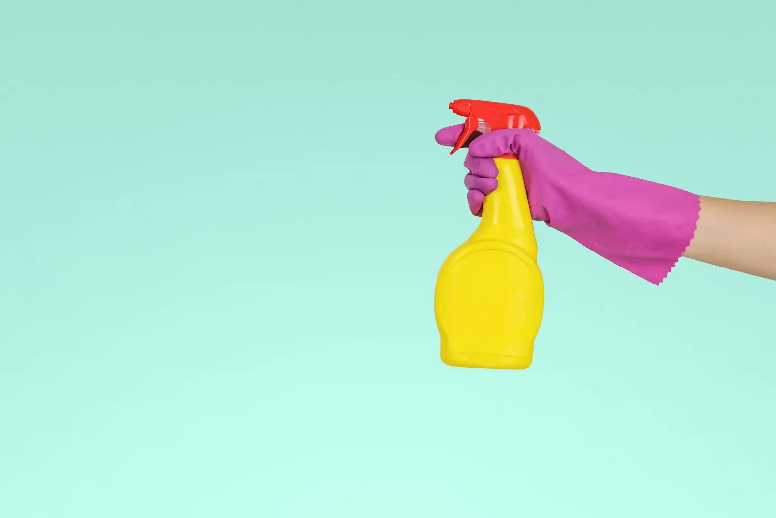 Mano con guante sosteniendo un atomizador amarillo